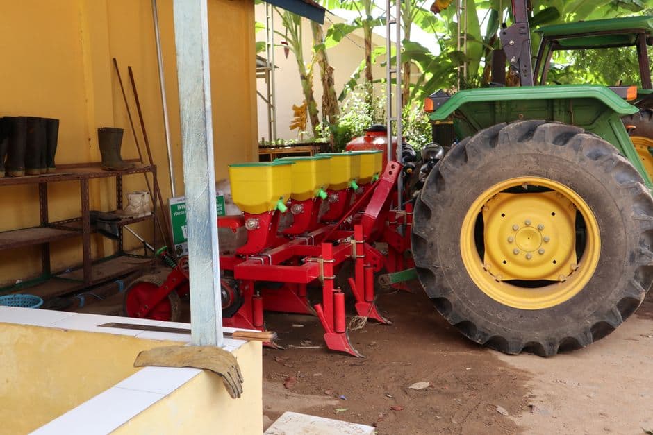 A red four-row planter hitched to a green tractor under a farm shed roof.