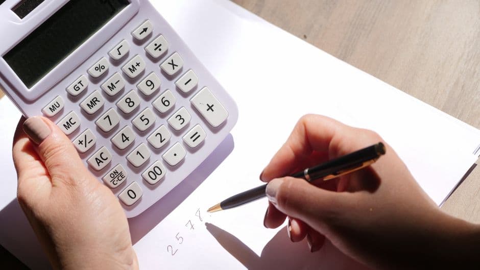 Hands holding a calculator and writing figures on a sheet of paper.