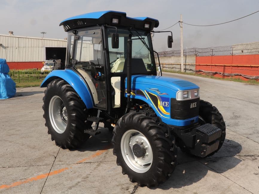 A new blue four-wheel-drive tractor with a cab, parked on a concrete yard.