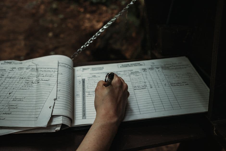 A hand writing entries into the ruled columns of a logbook.