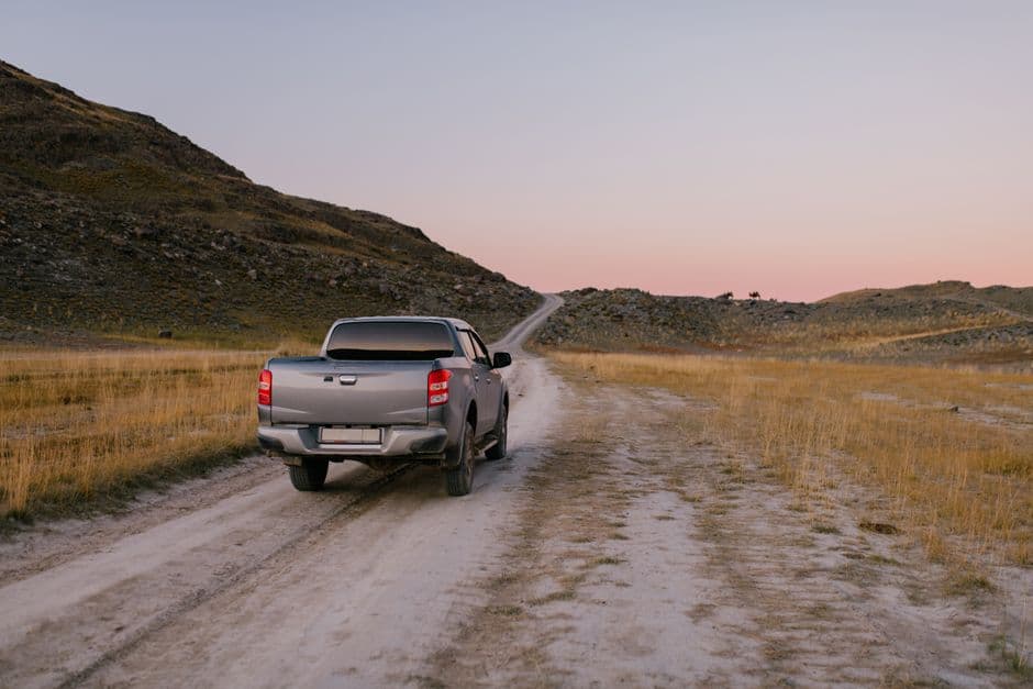 A pickup truck on a gravel track through dry grassland at dusk.